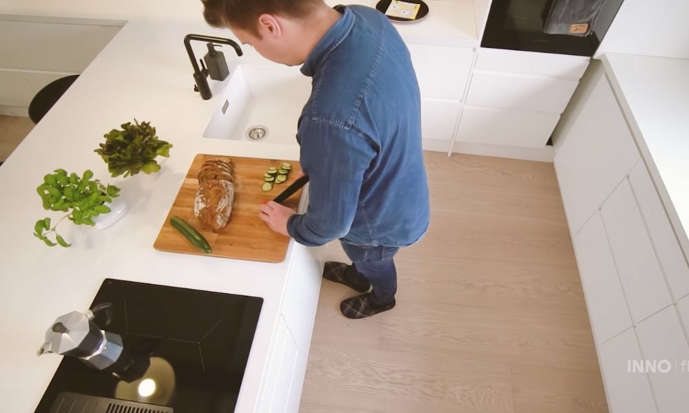 Keittiön lattialla seisten työskentelevä mies leikkaa leipää.